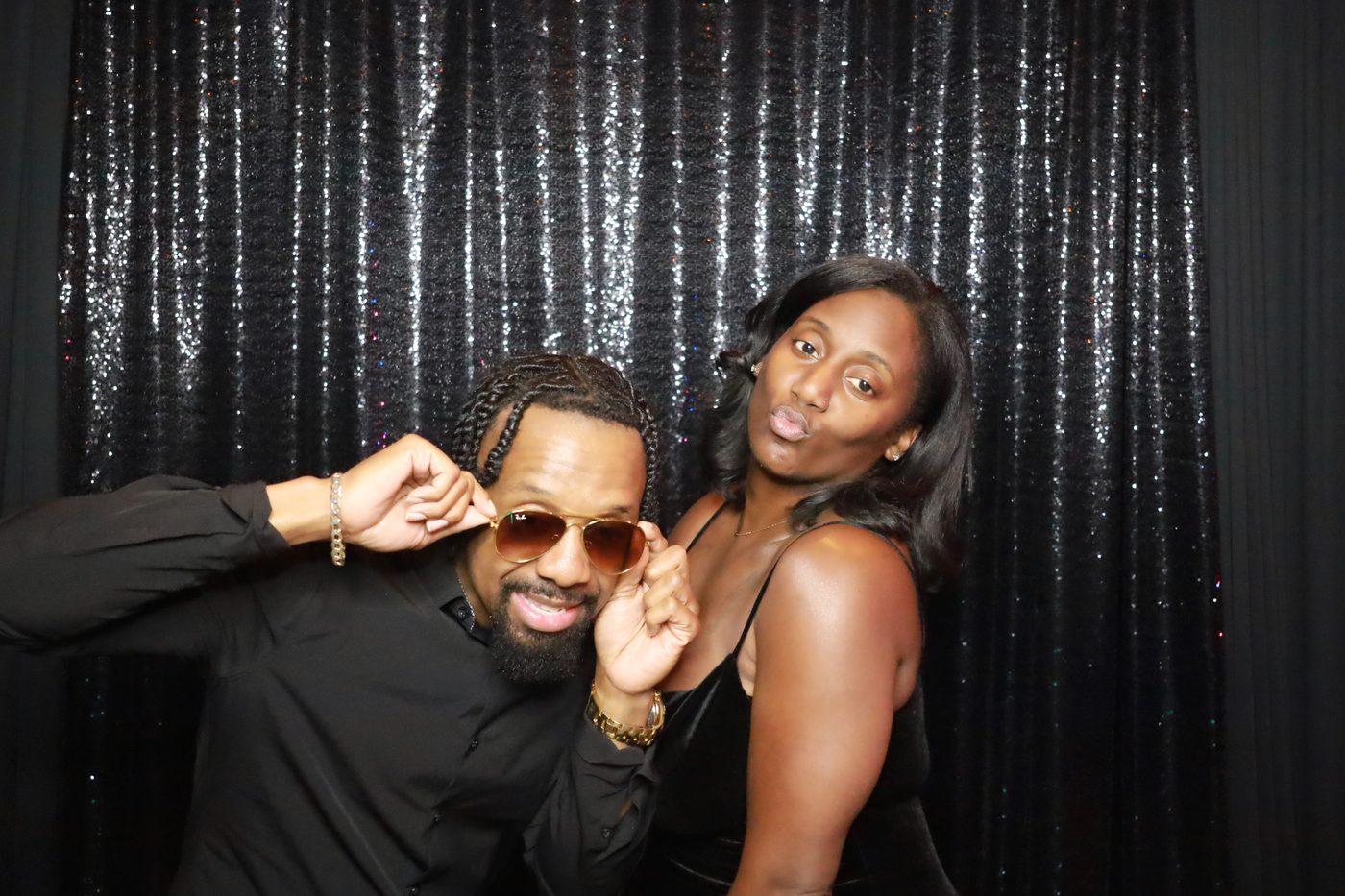 Couple posing with sunglasses at a sequin backdrop photo booth