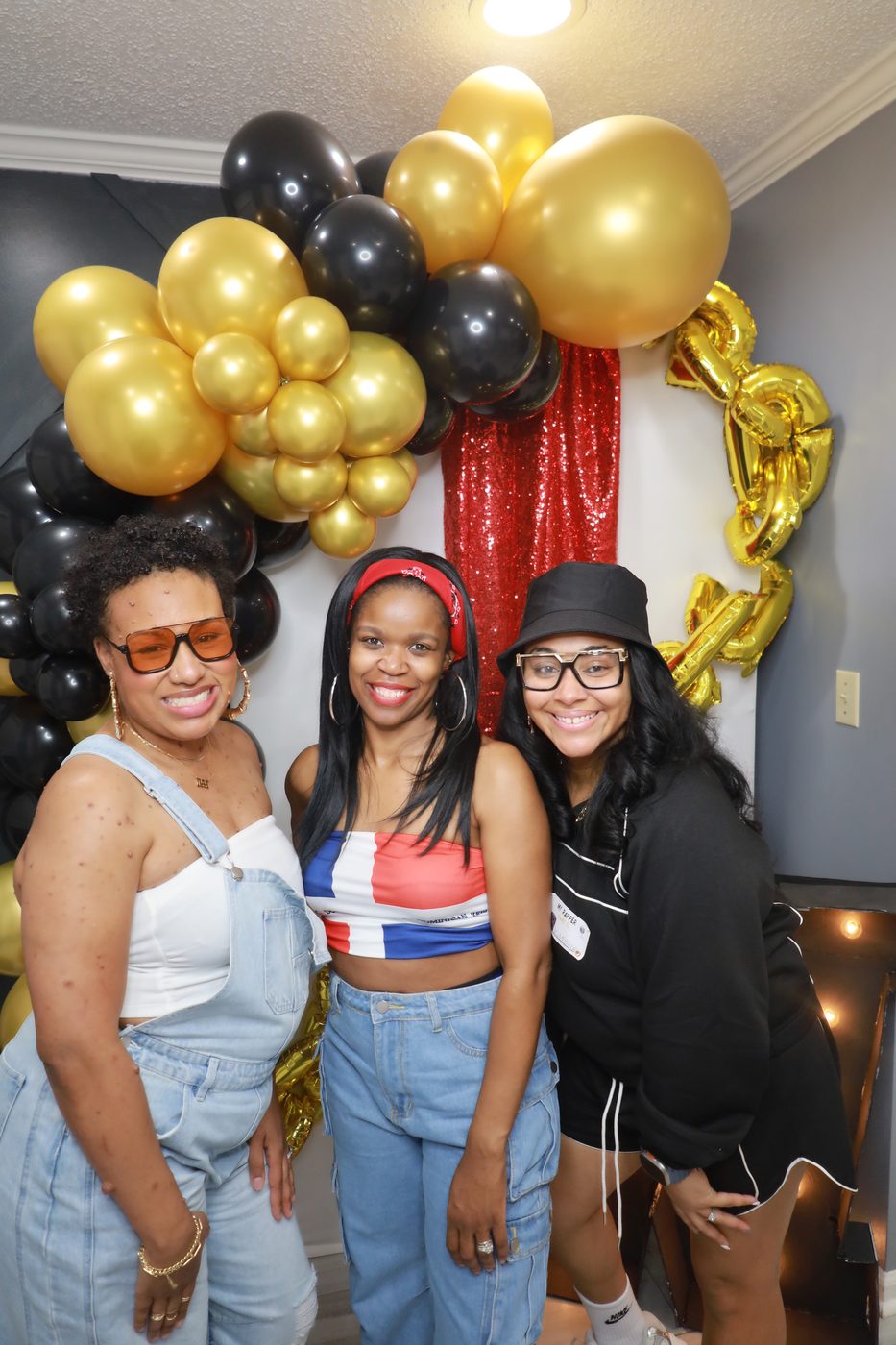 Three friends at a birthday party photo booth with balloon arch